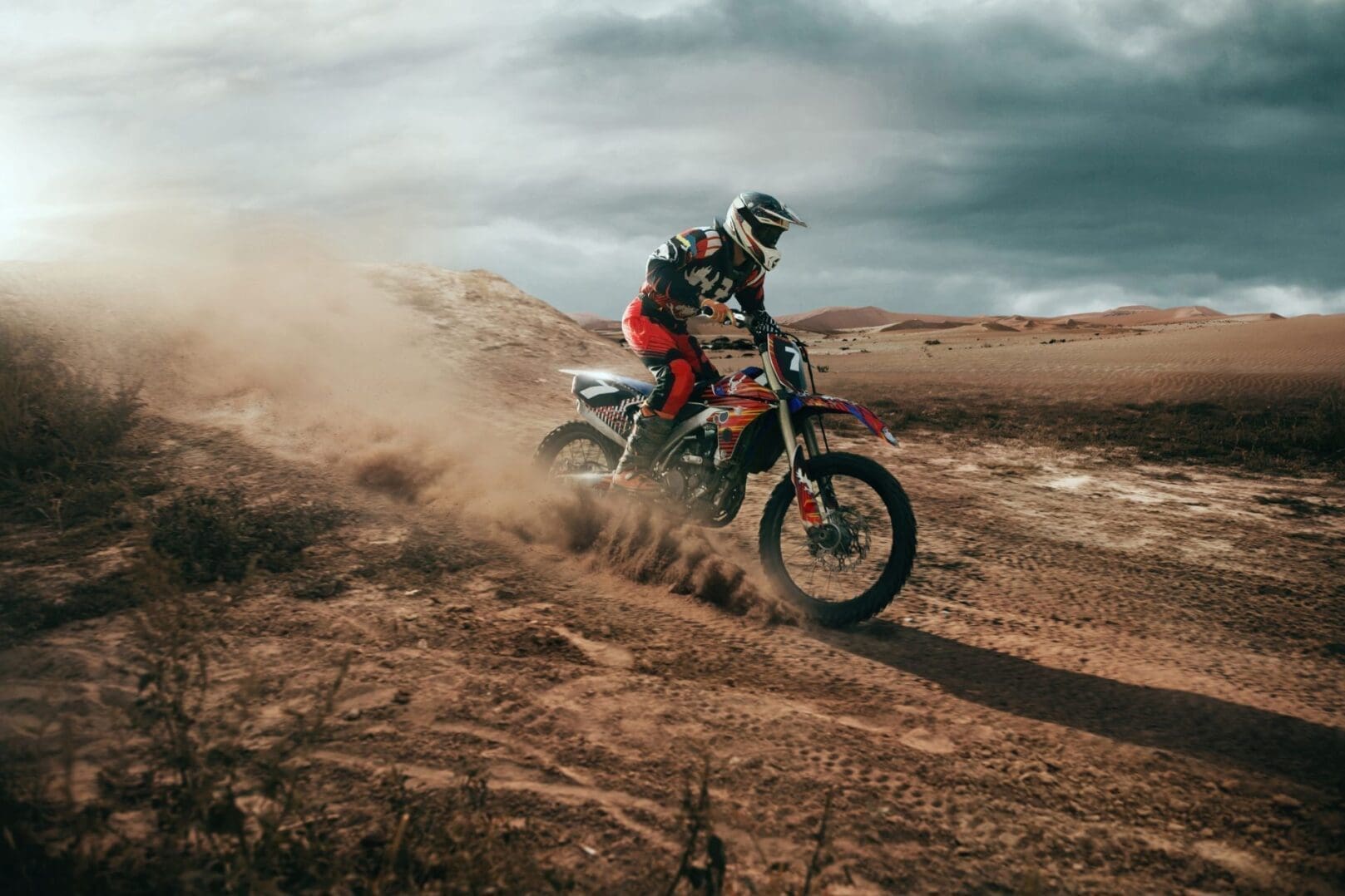 Motorcyclist riding through desert landscape, kicking dust.